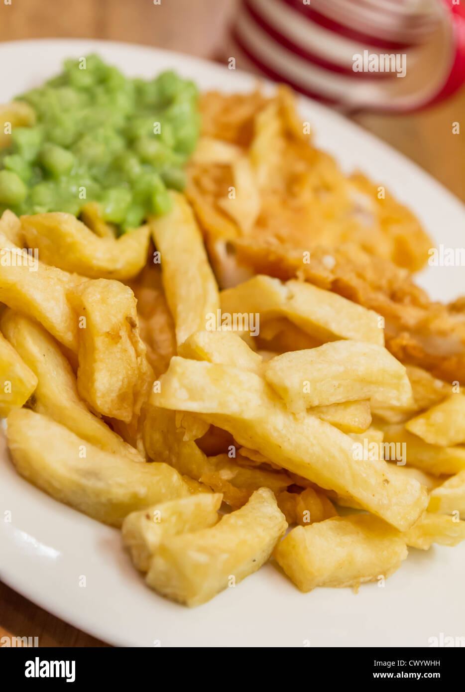 A plate of traditionally fried fish and chips with mushy peas and a mug