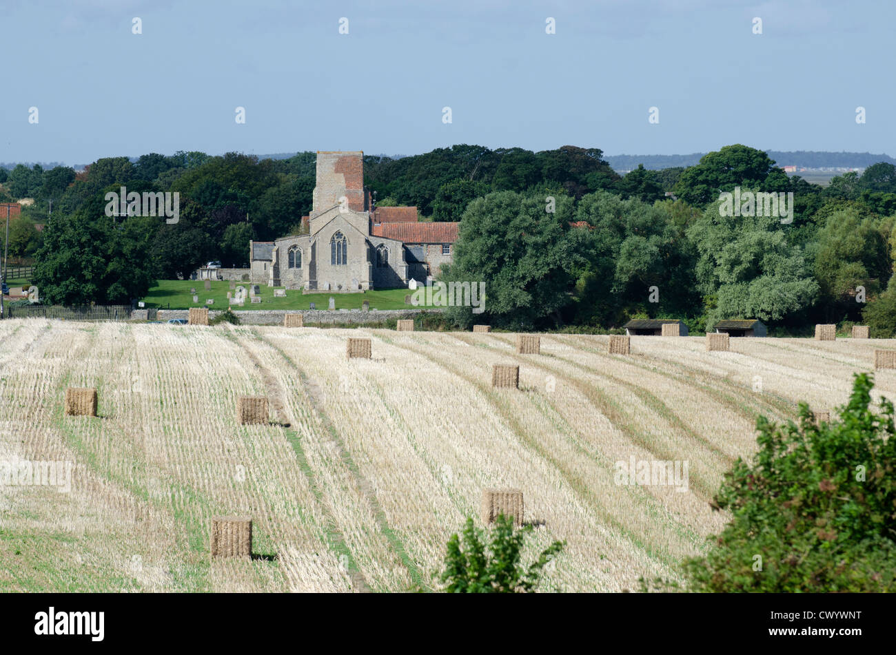 Harvested stubble field with bales, Morston All Saints Church in background, Norfolk, England Stock Photo