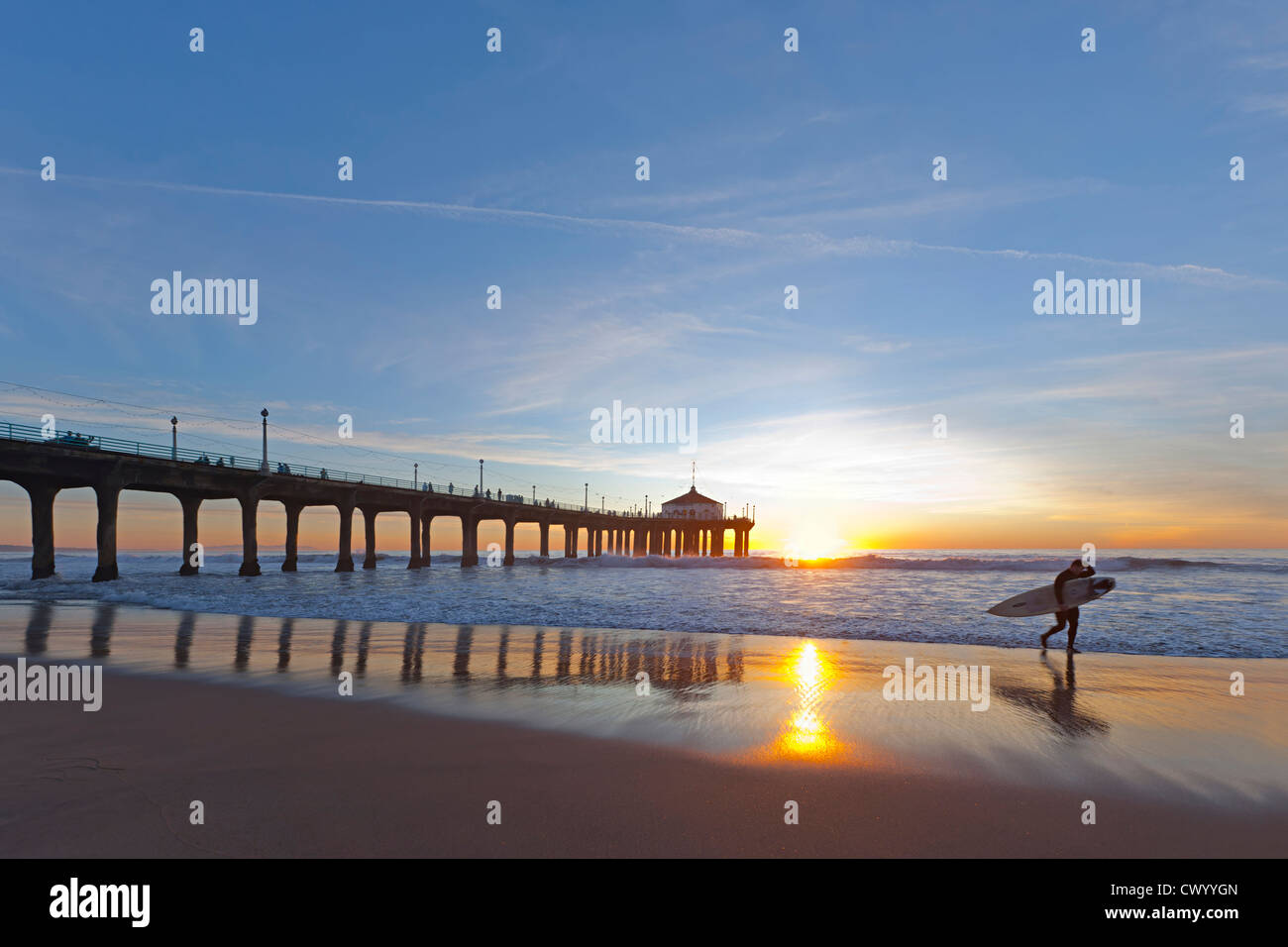 Surfer walks out of the sea in front the pier and sunset at Manhattan beach, California, USA Stock Photo