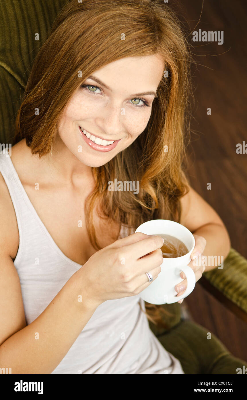 Smiling young woman drinking tea in armchair Stock Photo