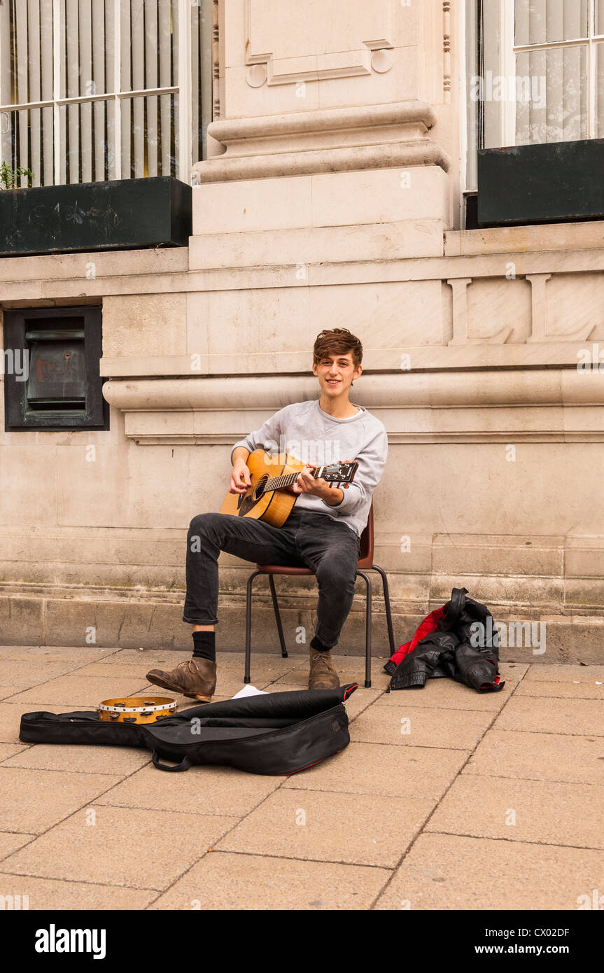 A young man busking with his guitar in Norwich , Norfolk , England , Britain , Uk Stock Photo