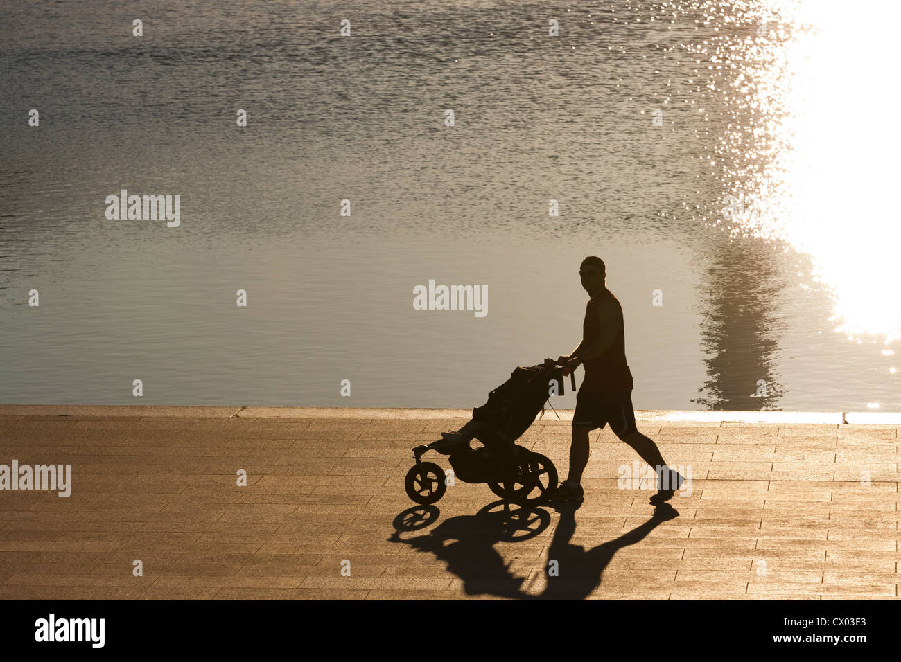 A man pushing a baby stroller in early morning light Stock Photo