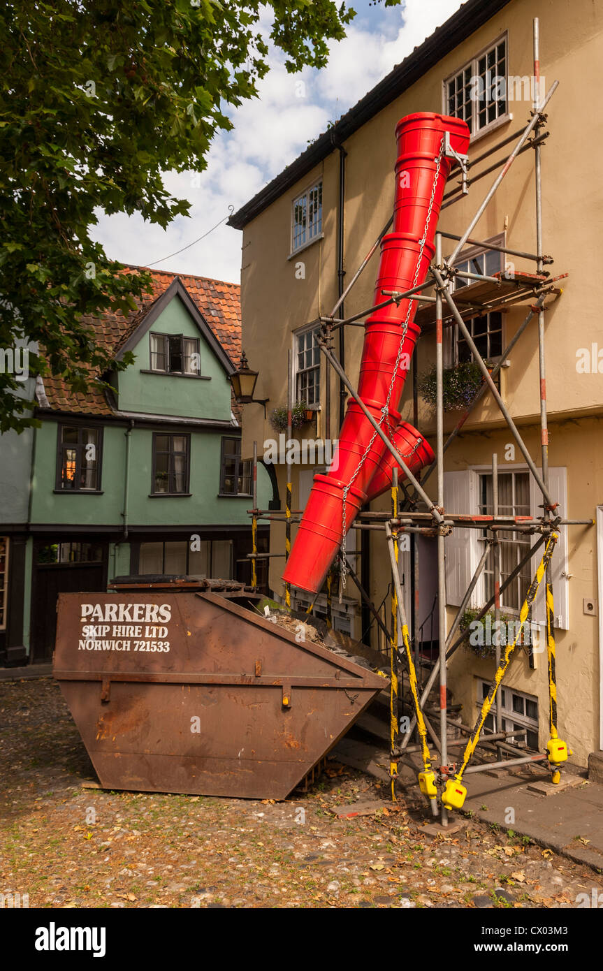 A builders rubbish chute goes into a skip in Norwich , Norfolk