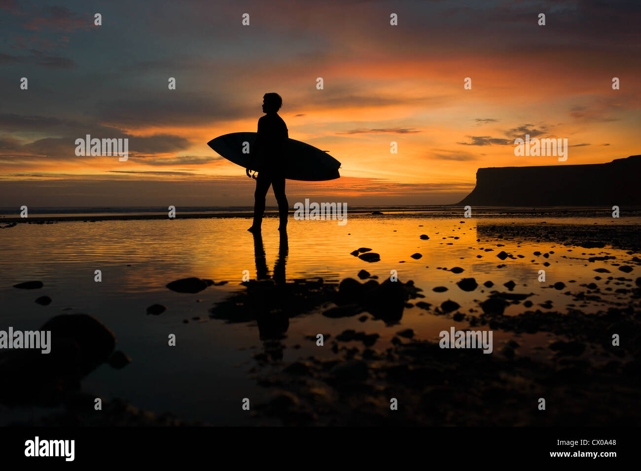 A surfer looks towards the morning surf at sunrise at Saltburn beach in