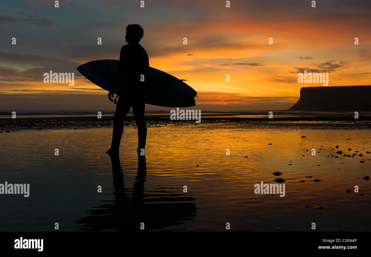 A surfer looks towards the morning surf at sunrise at Saltburn beach in