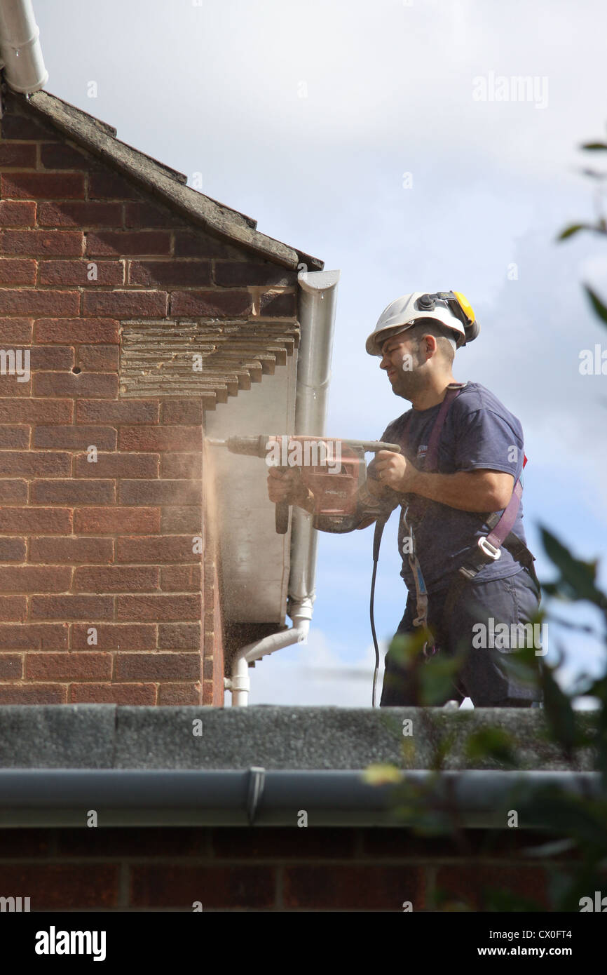 Workman drilling holes in a suburban house wall in preparation for