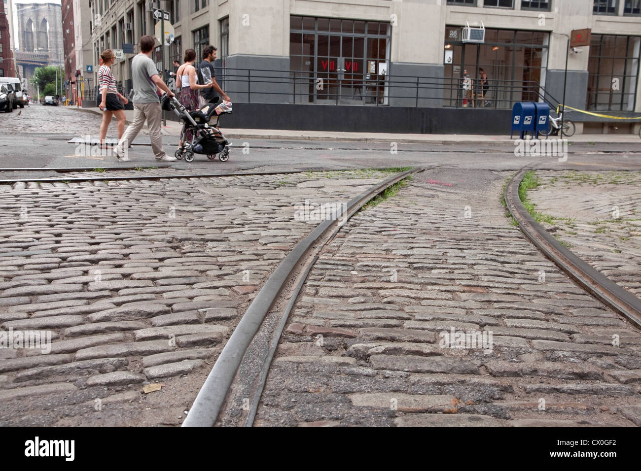 Tourists stroll along old cobblestone streets & trolley tracks in the DUMBO section of Brooklyn, New York past VII Photo Agency. Stock Photo