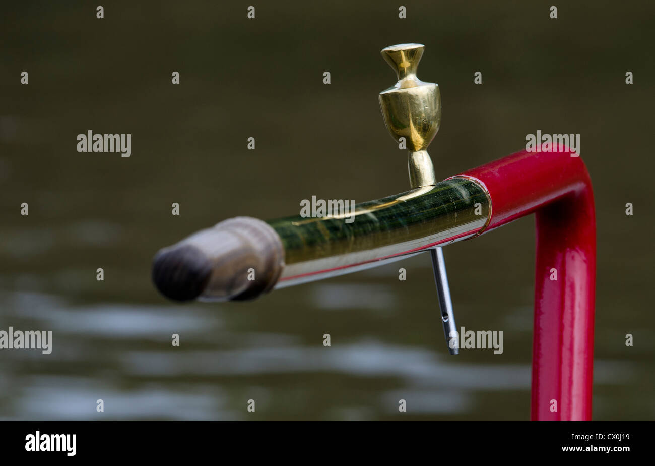 Tiller of traditional UK canal boat featuring brass tiller pin, with specular highlights on water in background Stock Photo