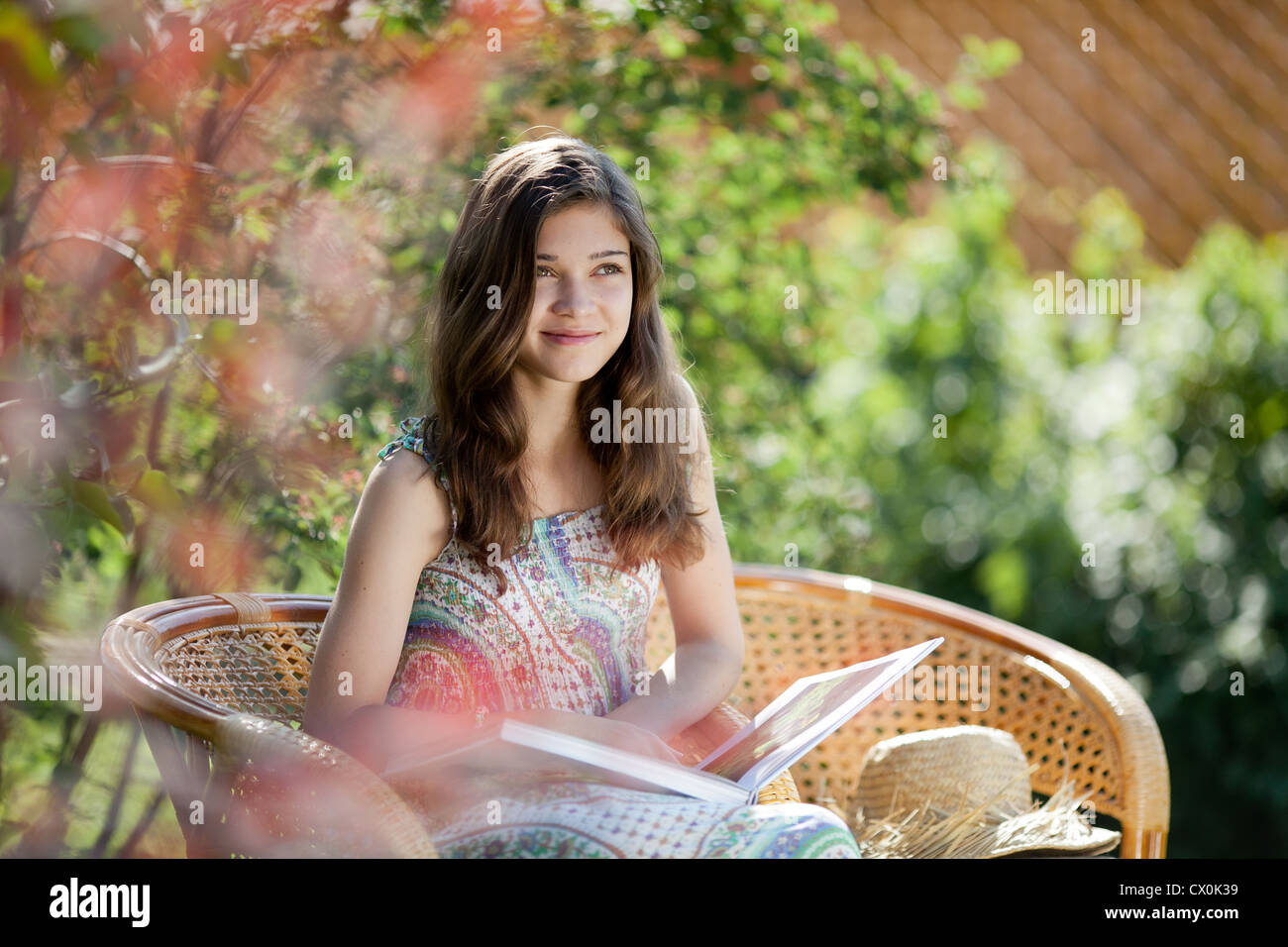 Girl reading book sitting in wicker chair outdoor in summer day Stock Photo