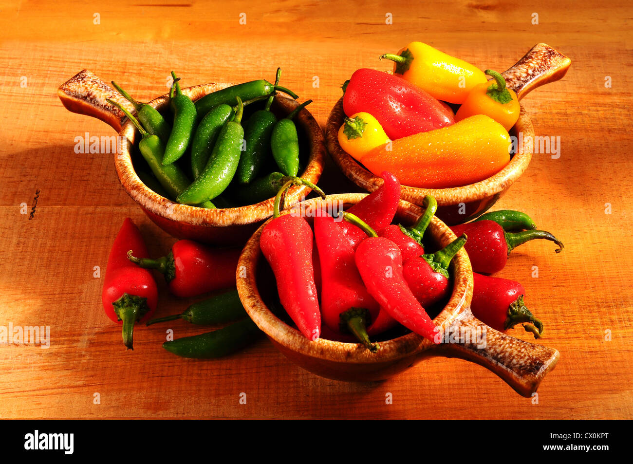 An assortment of Sweet Peppers and Chilies in Bowls on a rustic wooden surface. Stock Photo