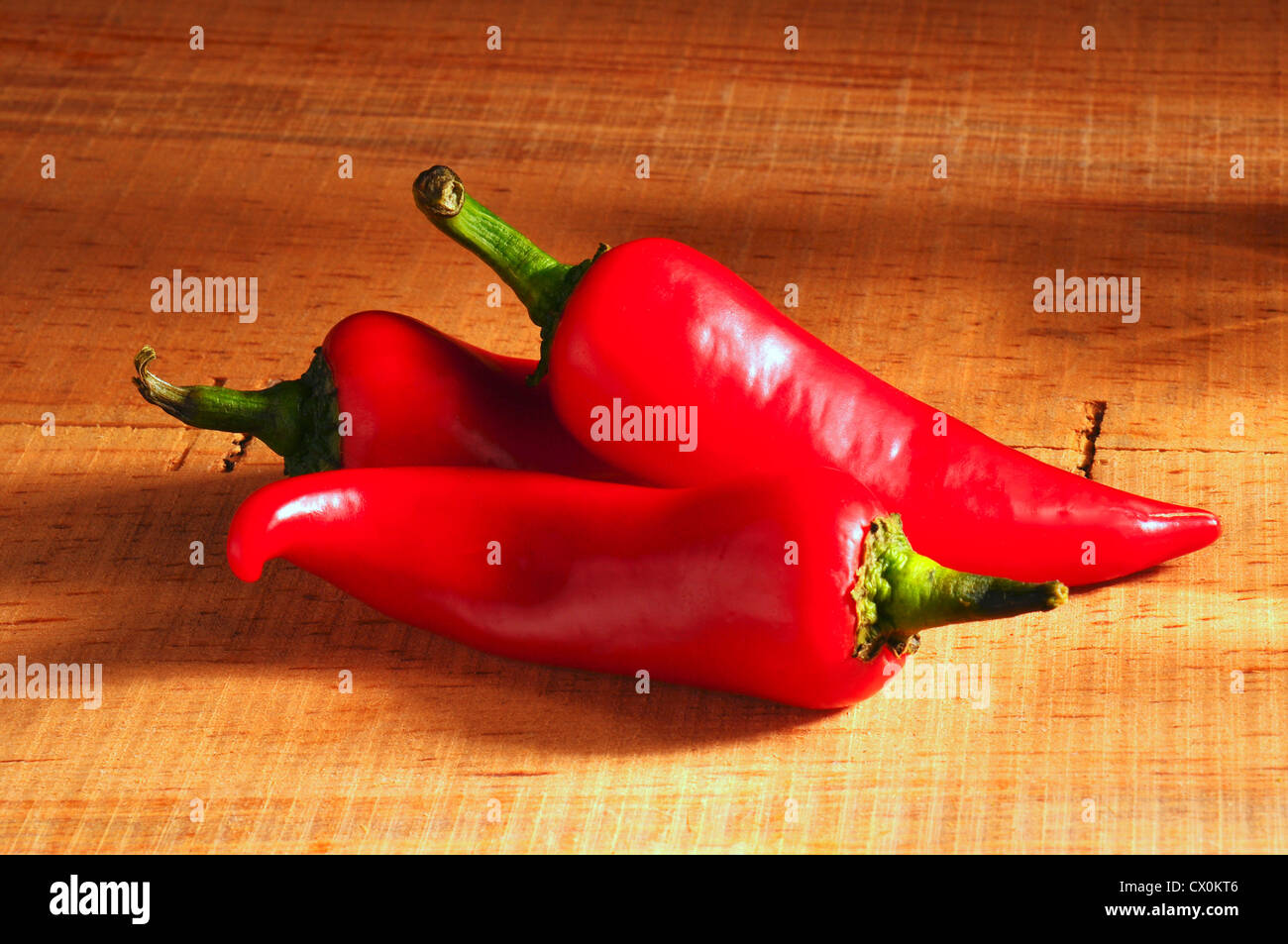 Closeup of three red peppers on rustic wood table. Stock Photo