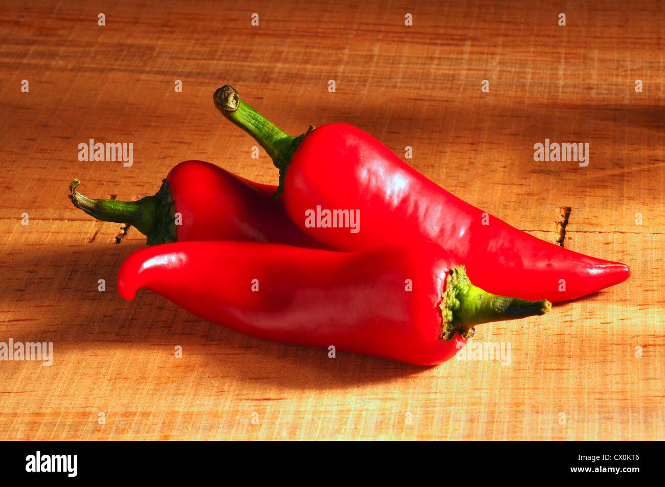Closeup of three red peppers on rustic wood table Stock Photo - Alamy
