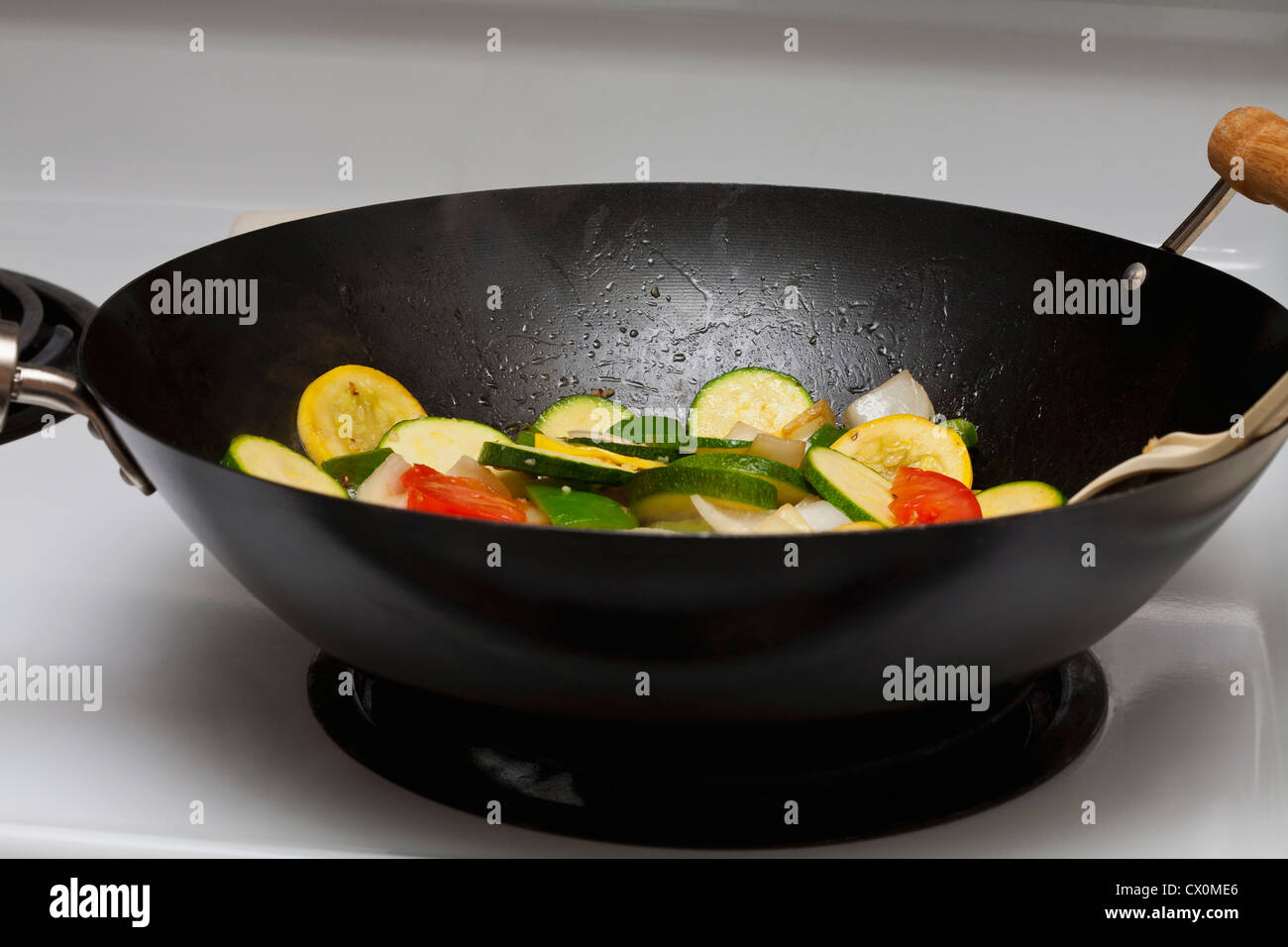 Yellow squash, zucchini, tomatoes, onions and garlic cooking in a Chinese wok. Stock Photo