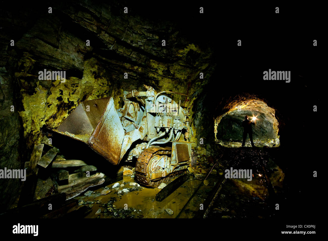A person exploring a mine, with a digger in the foreground Stock Photo