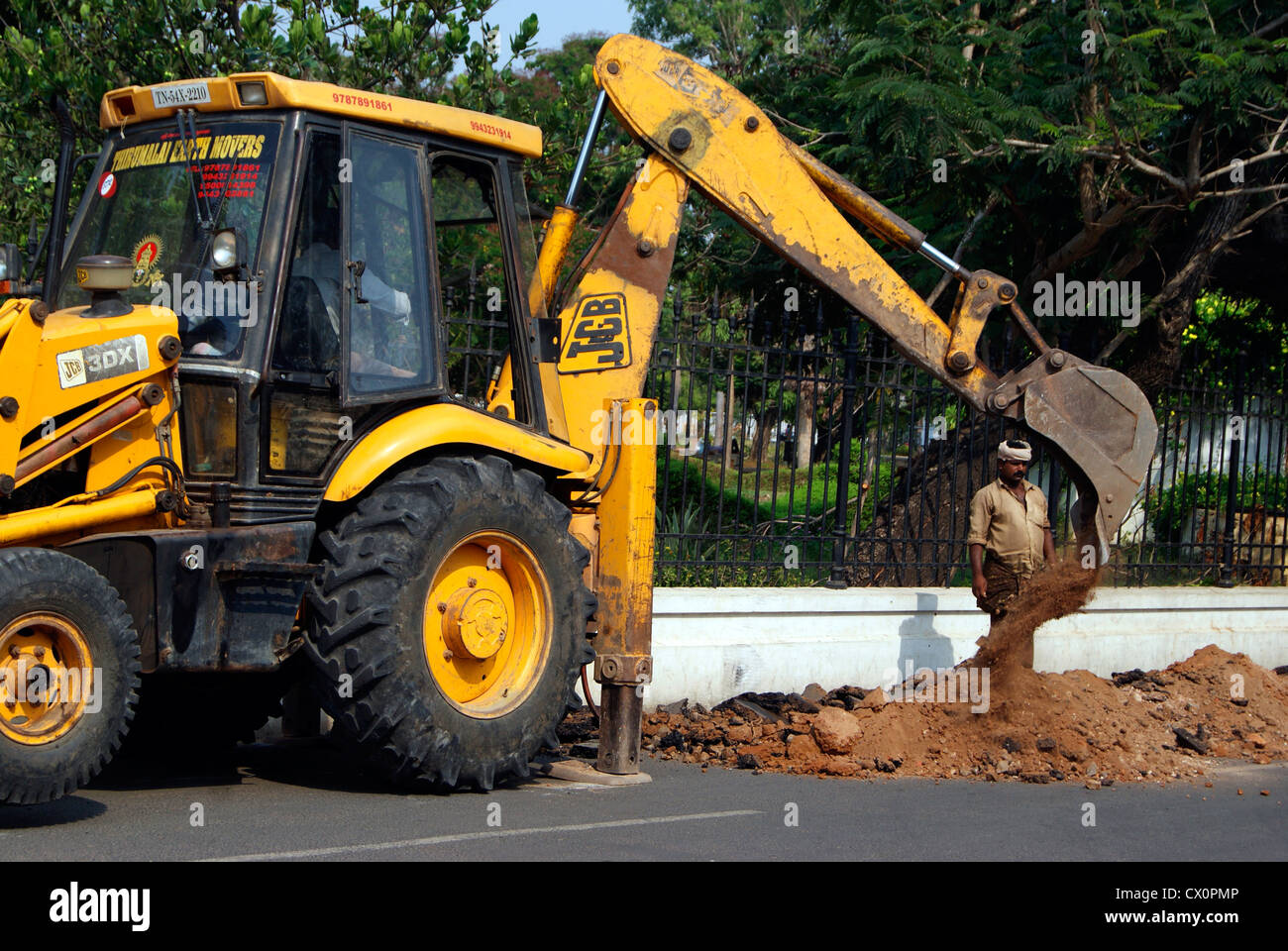 JCB Digger Digging Earth from Tarred Road in Pondicherry Town in India for Maintenance works Stock Photo