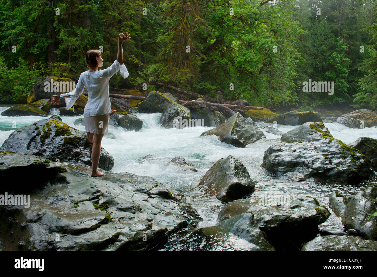 Woman meditating on rock by water Stock Photo