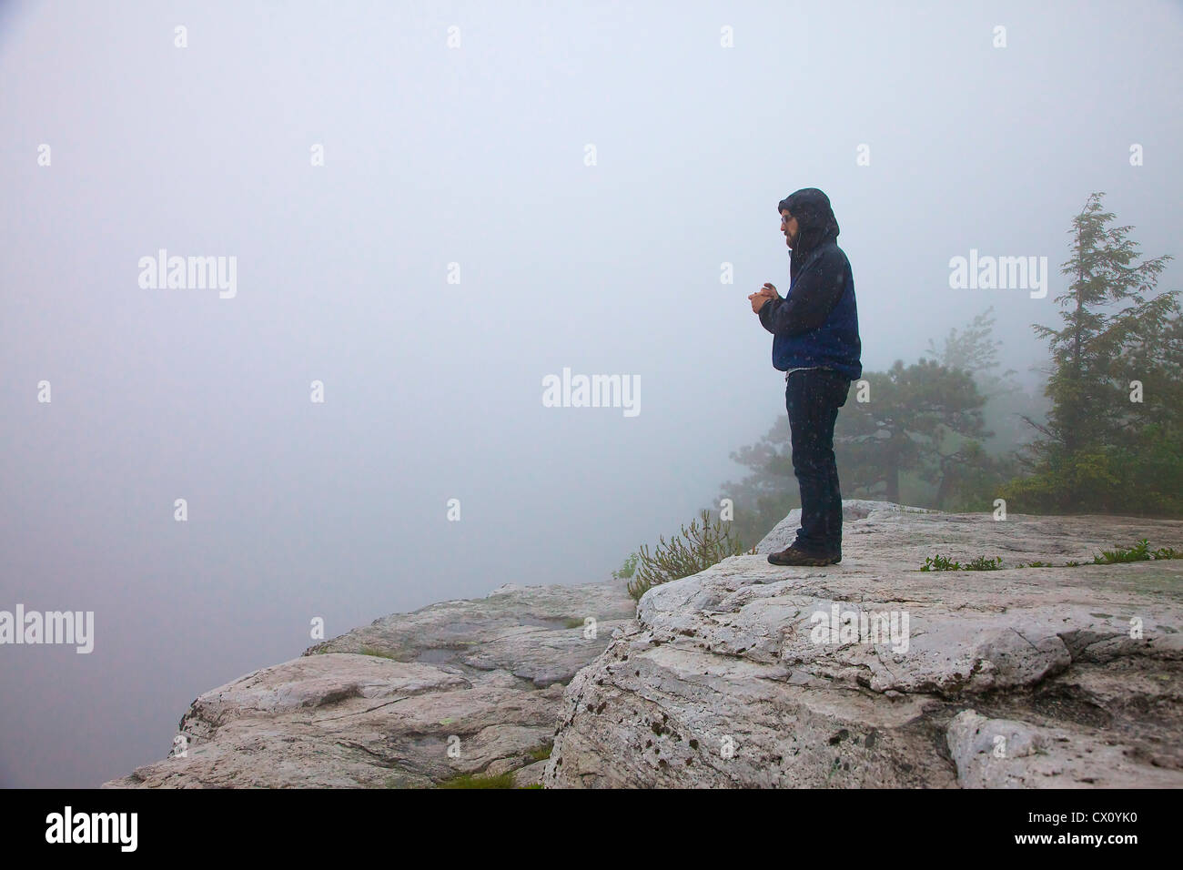 Man on a cliff in the rain and fog Stock Photo