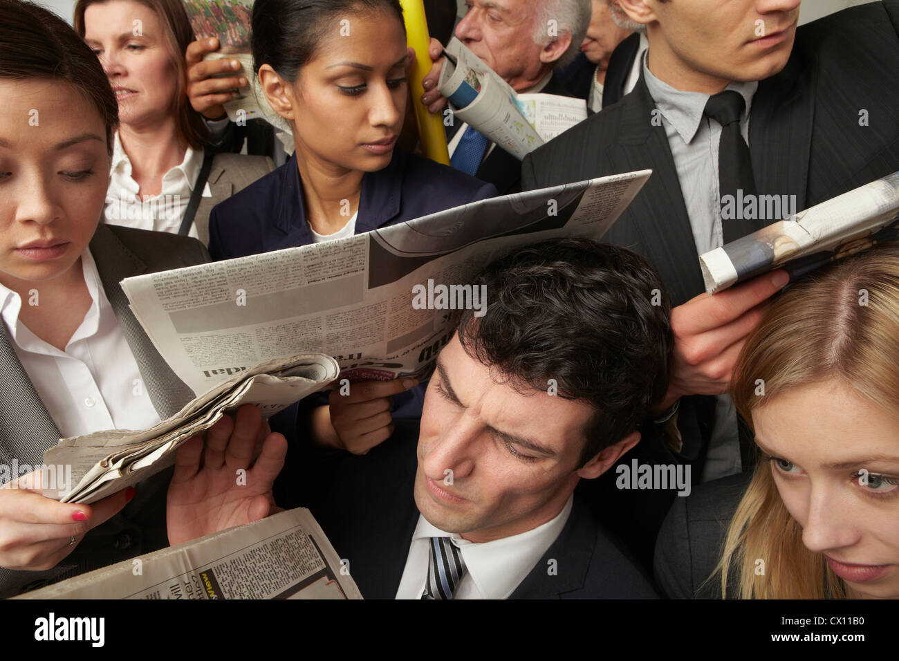 Businesspeople reading newspapers on crowded train Stock Photo