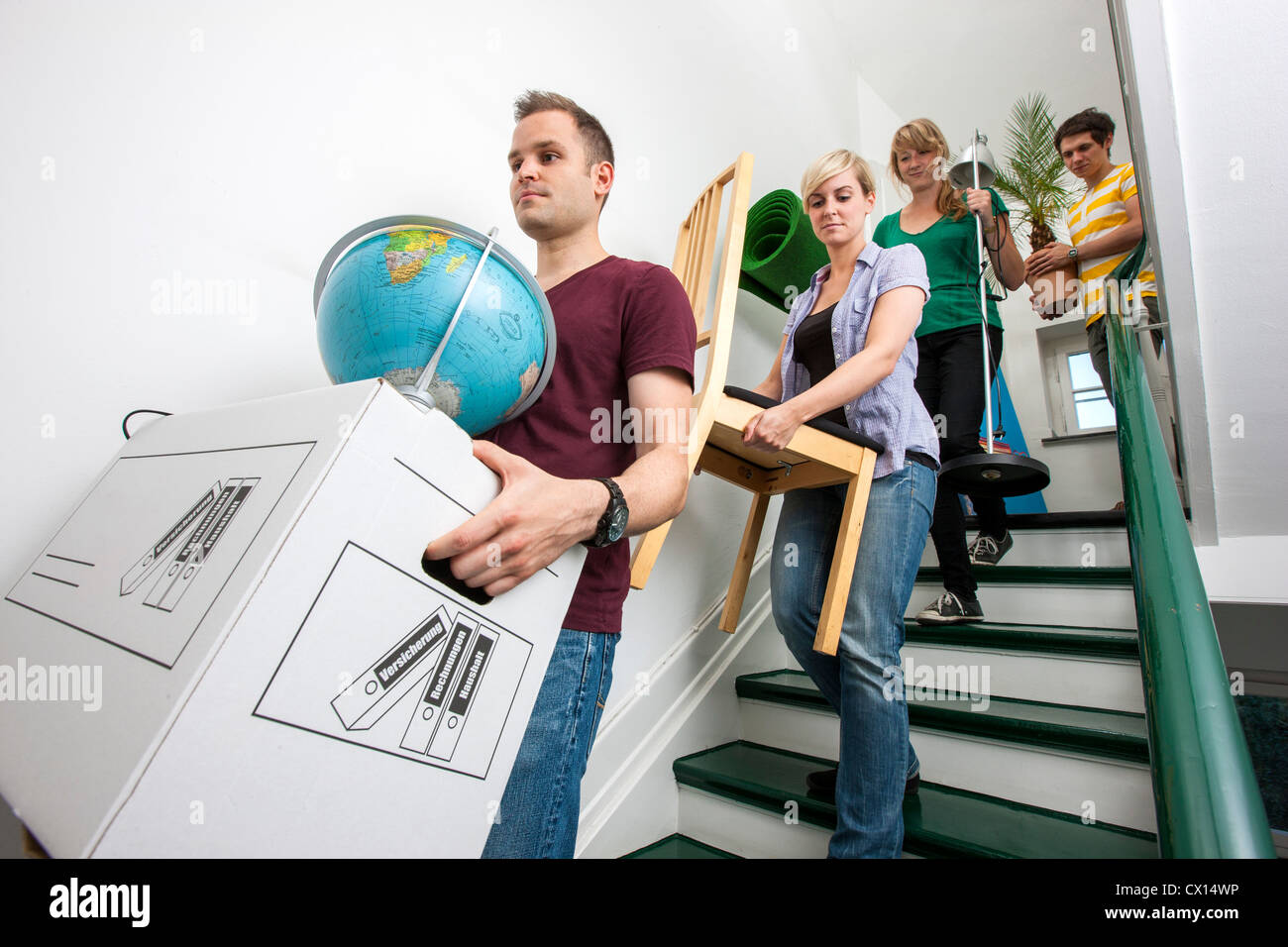 Young people moving in to a new apartment. Friends help carrying moving boxes, furniture and things upstairs to the new flat. Stock Photo
