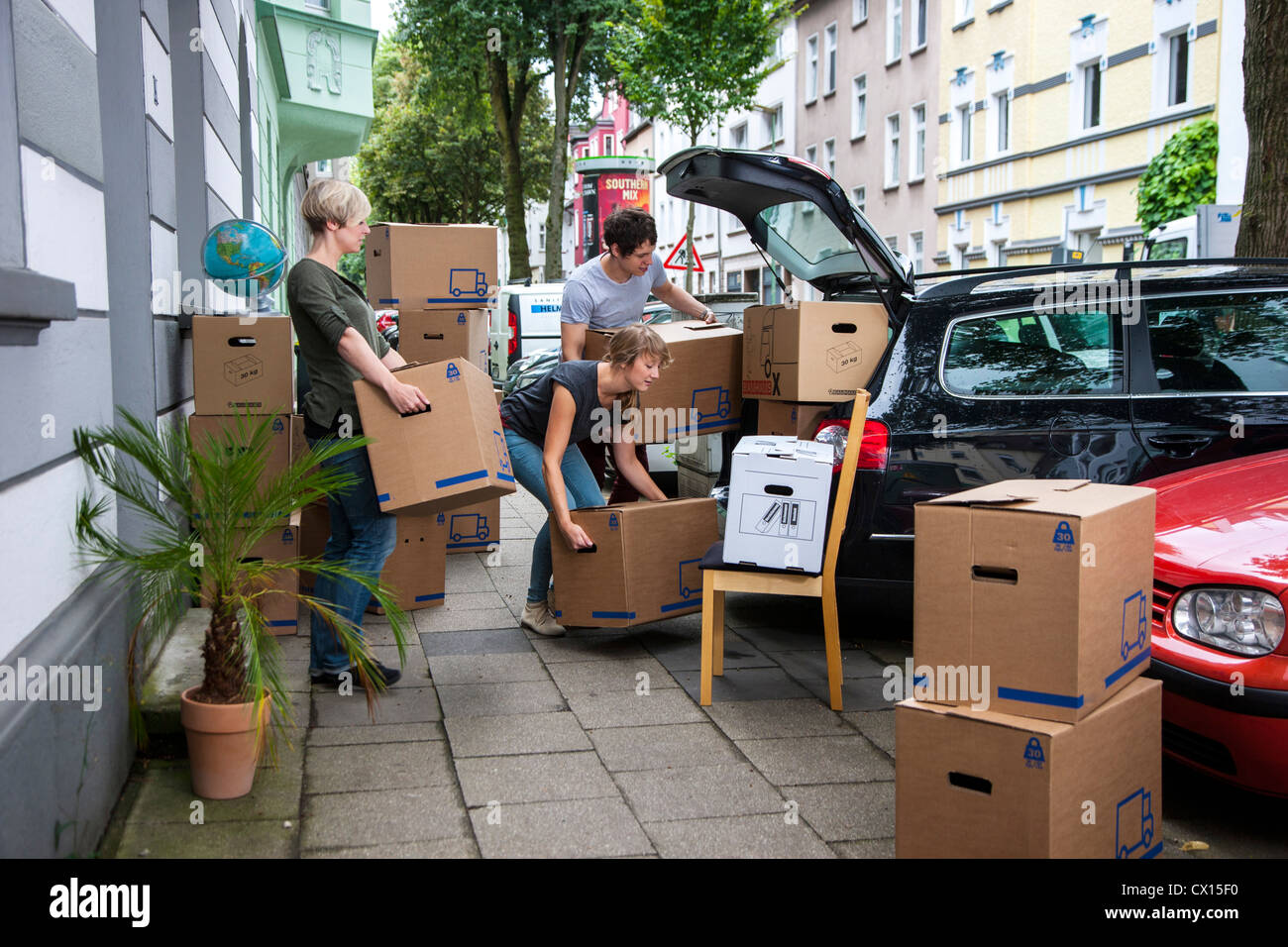 Moving into a new apartment. Friends help carrying moving boxes, furniture, things, from a car into the new house. Stock Photo