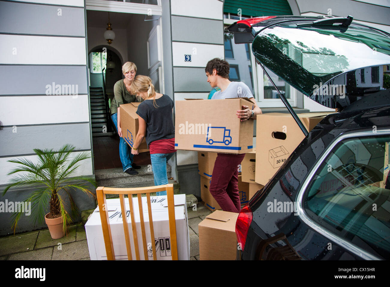 Moving into a new apartment. Friends help carrying moving boxes, furniture, things, from a car into the new house. Stock Photo