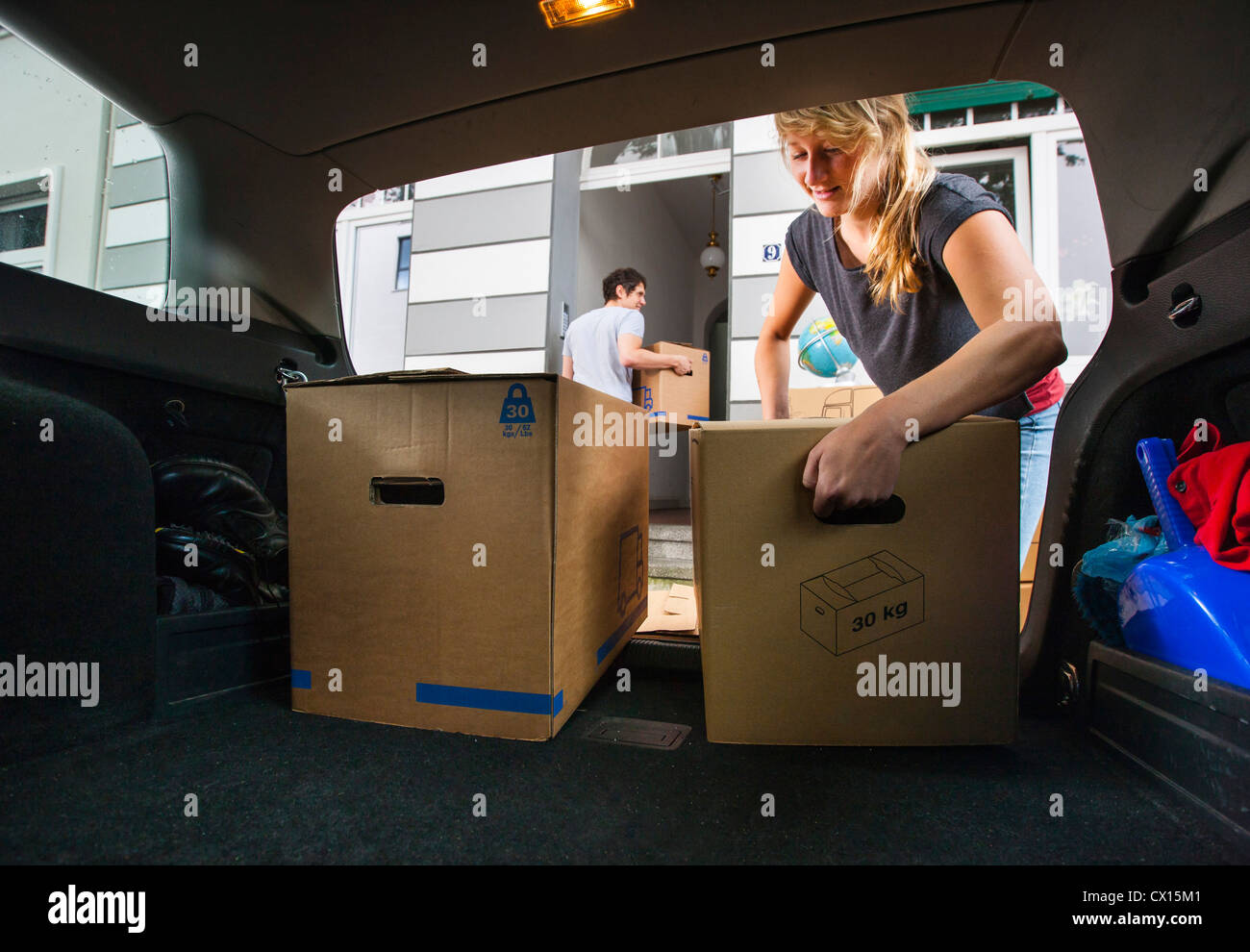 Moving into a new apartment. Friends help carrying moving boxes, furniture, things, from a car into the new house. Stock Photo