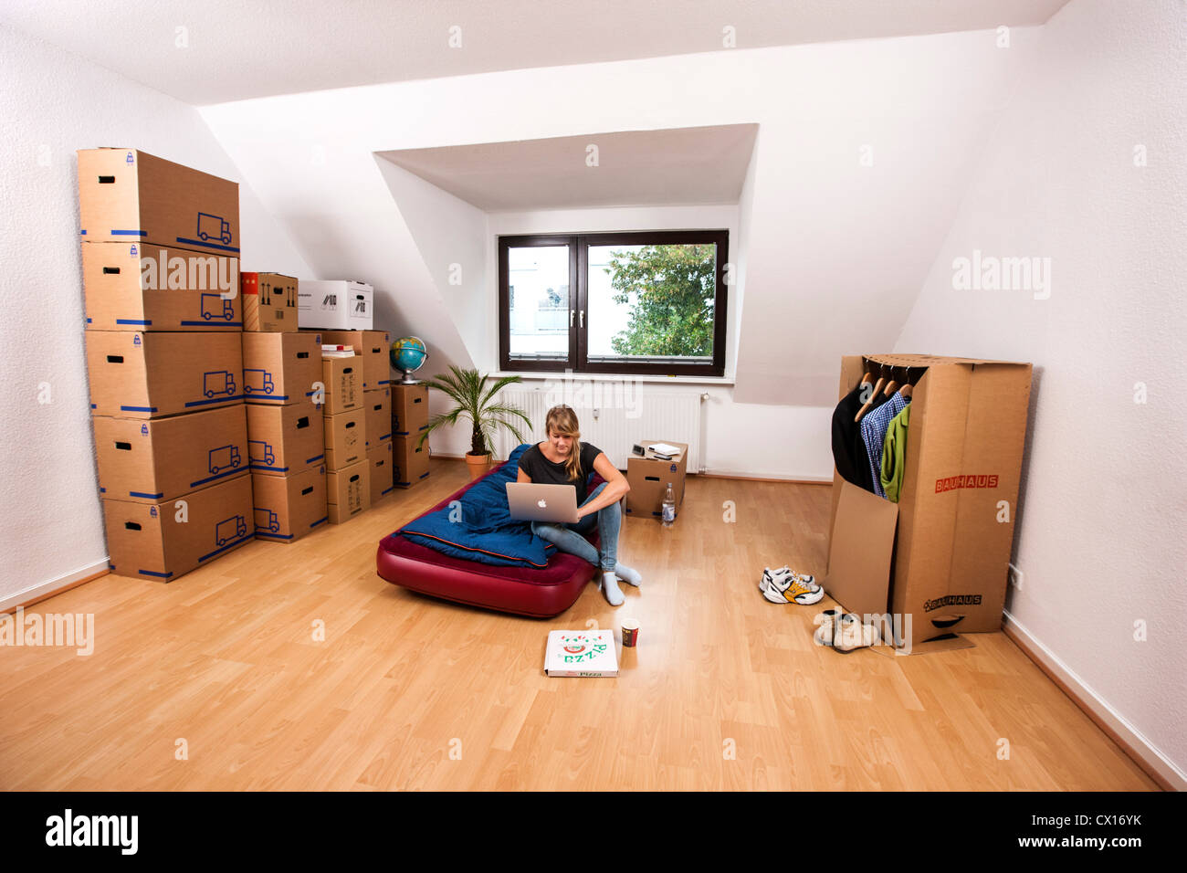 Young woman in her new apartment. Still no furniture. Living out of moving boxes. Works with her Laptop computer. Stock Photo