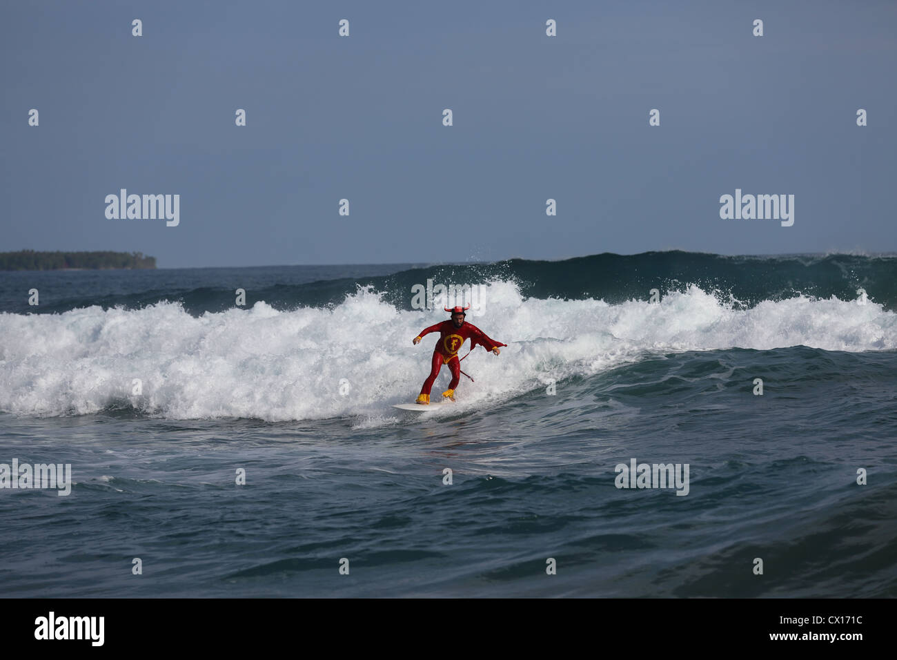 Surfer dressed in red devil super hero costume surfing a wave in Krui, South Sumatra. Stock Photo