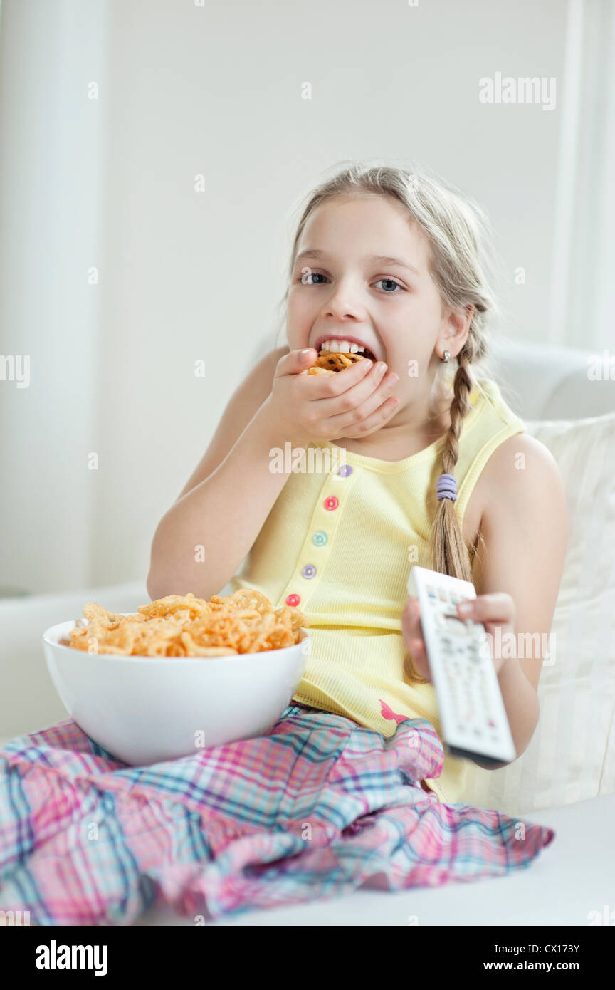 Girl watching TV as she stuffs her mouth with wheel shape snack pellets ...