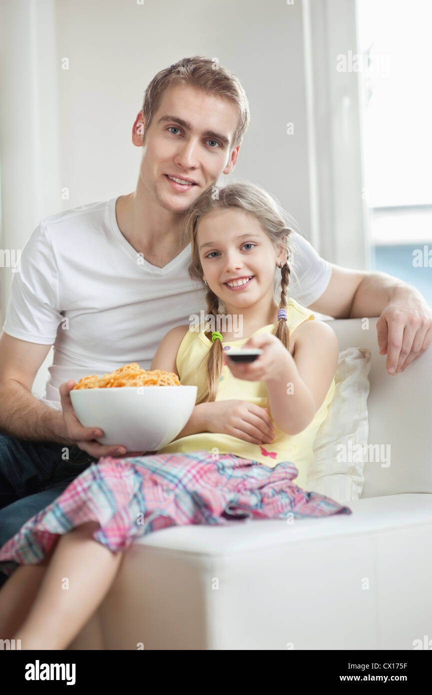 Portrait of father and daughter watching TV with bowl full of wheel shape snack pellets Stock Photo