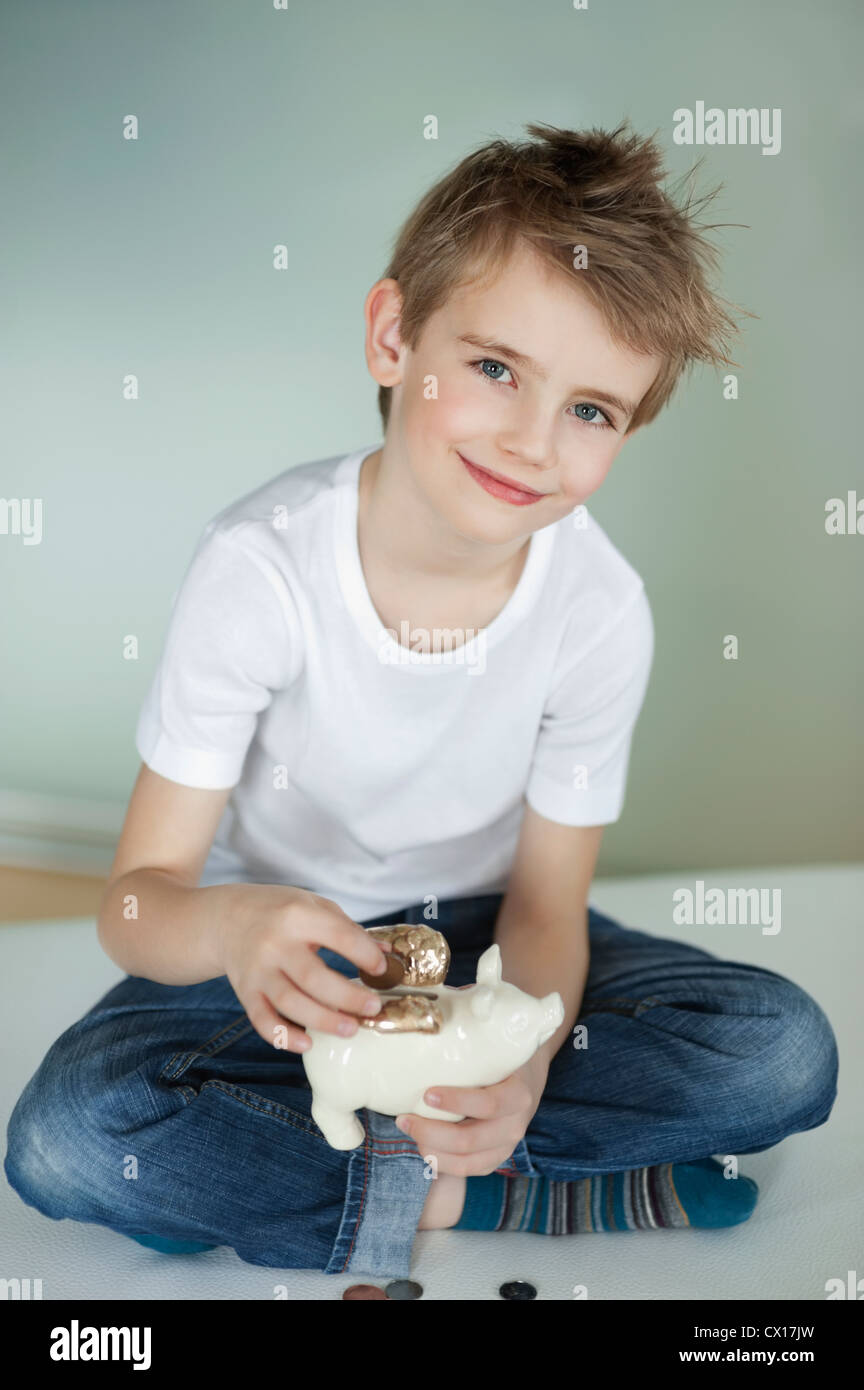 Portrait of young boy putting coin in piggy bank Stock Photo - Alamy