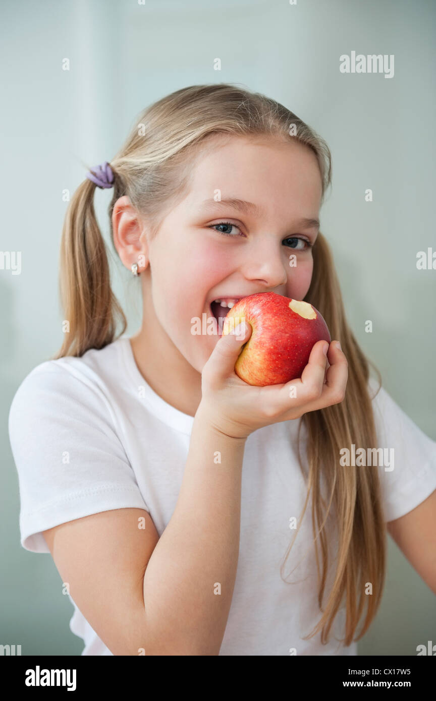 Portrait of happy young girl eating an apple over gray background Stock