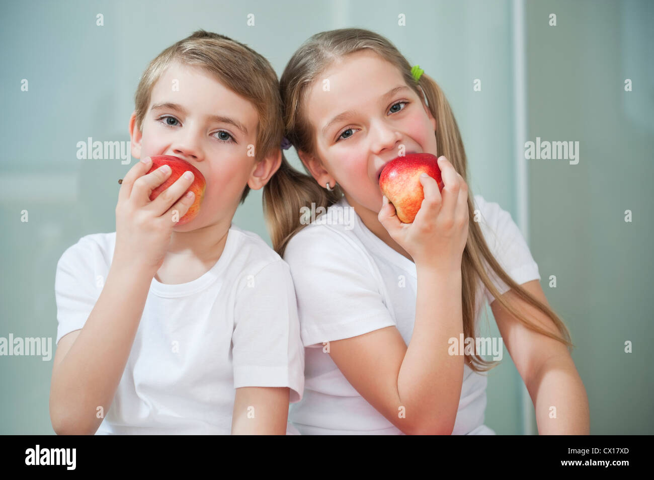 Portrait of young boy and girl in white tshirts eating apples Stock Photo