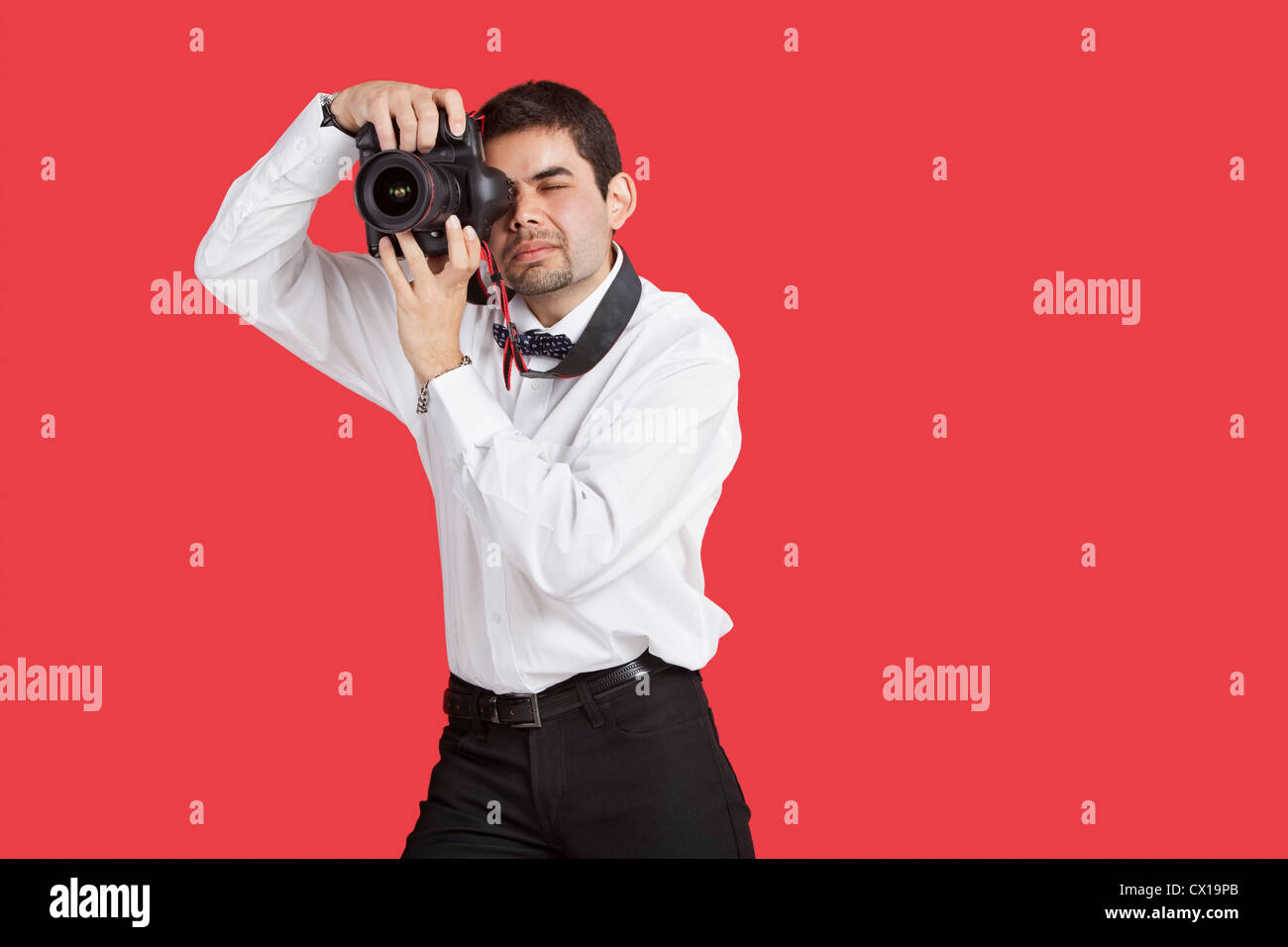 Mixed race man taking picture with digital camera over red background Stock Photo