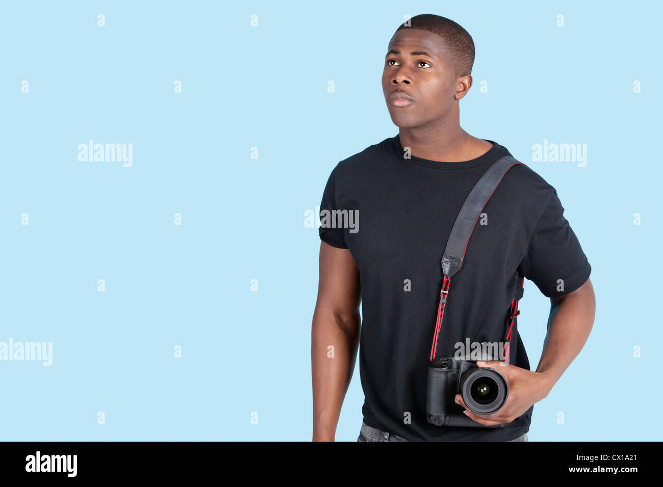 Young African American man with digital camera looking up over blue background Stock Photo