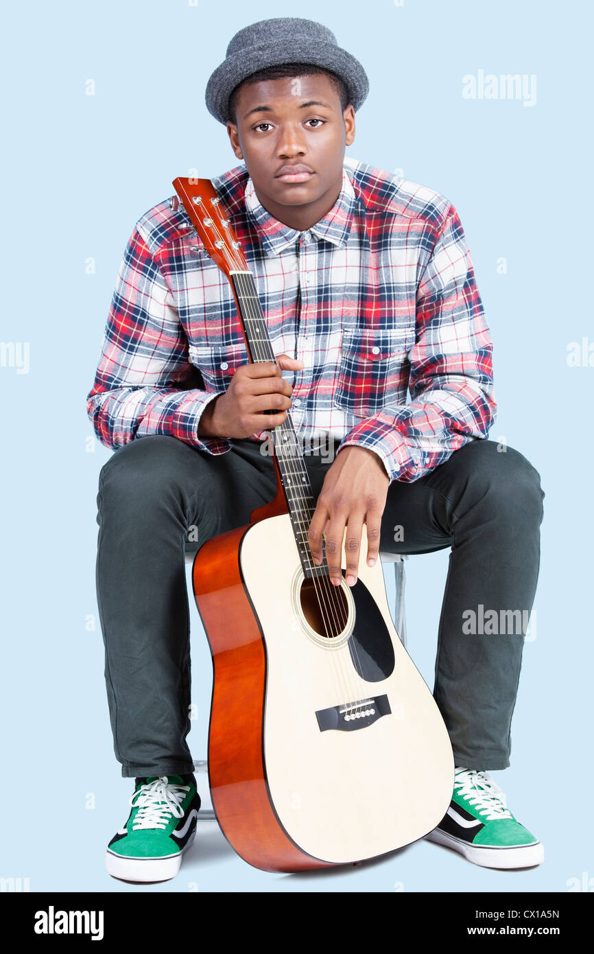 Portrait of a young African American man with guitar over light blue ...