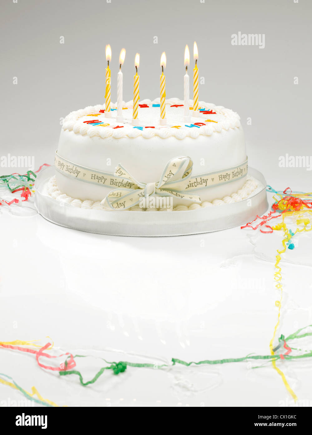 A white birthday cake with light candles and streamers Stock Photo