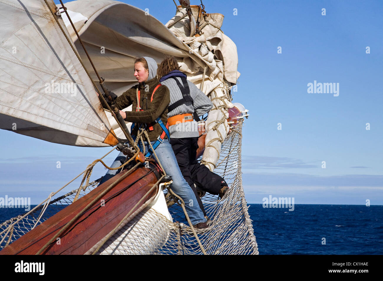 Sailors handling sails on bowsprit of the tall ship / barquentine Antigua sailing with tourists
