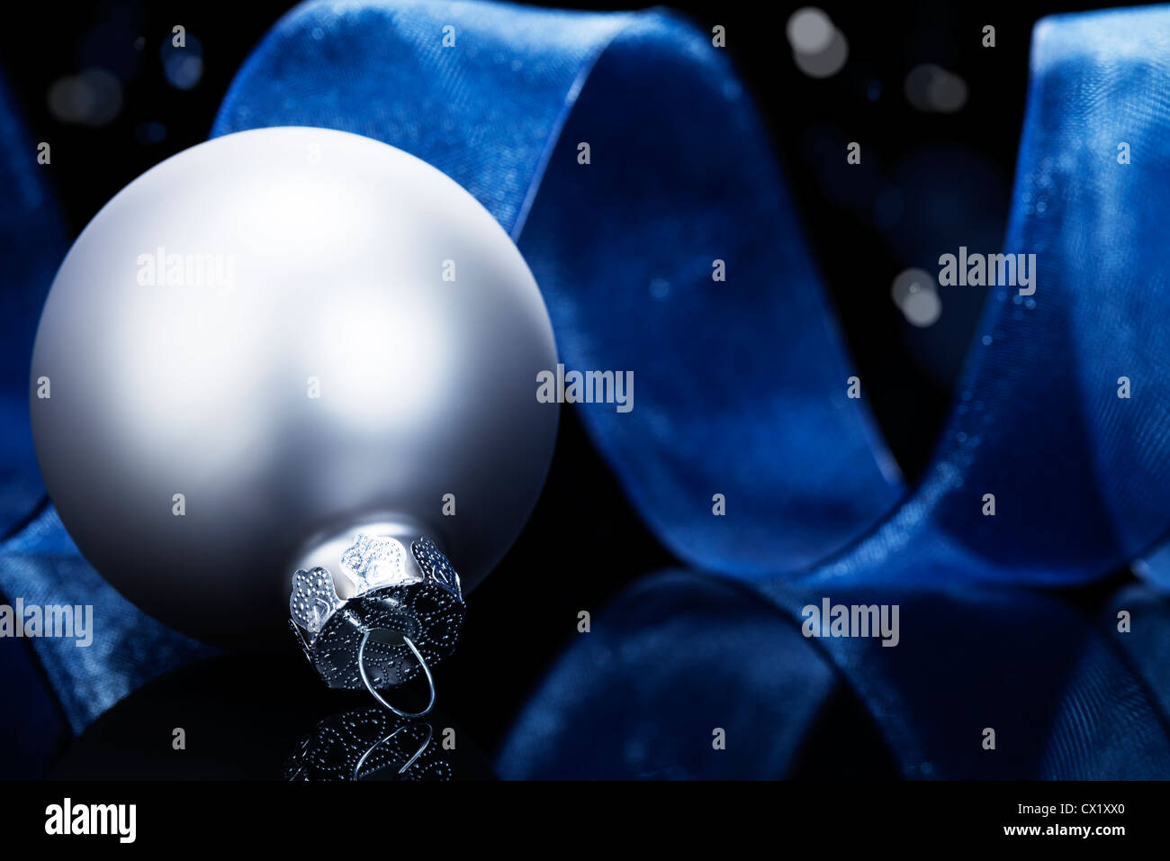 dull silver christmas ball in front of a blue ribbon on black ...