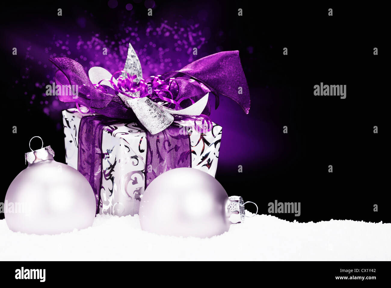 purple christmas present in snow with christmas balls and purple lightning on black background Stock Photo