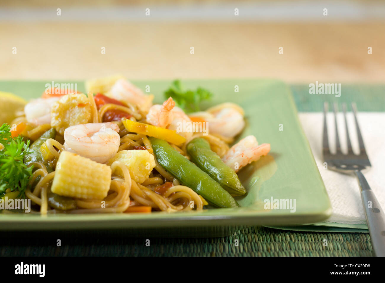 stir fry noodles with shrimp, snap peas, baby corn on a green plate