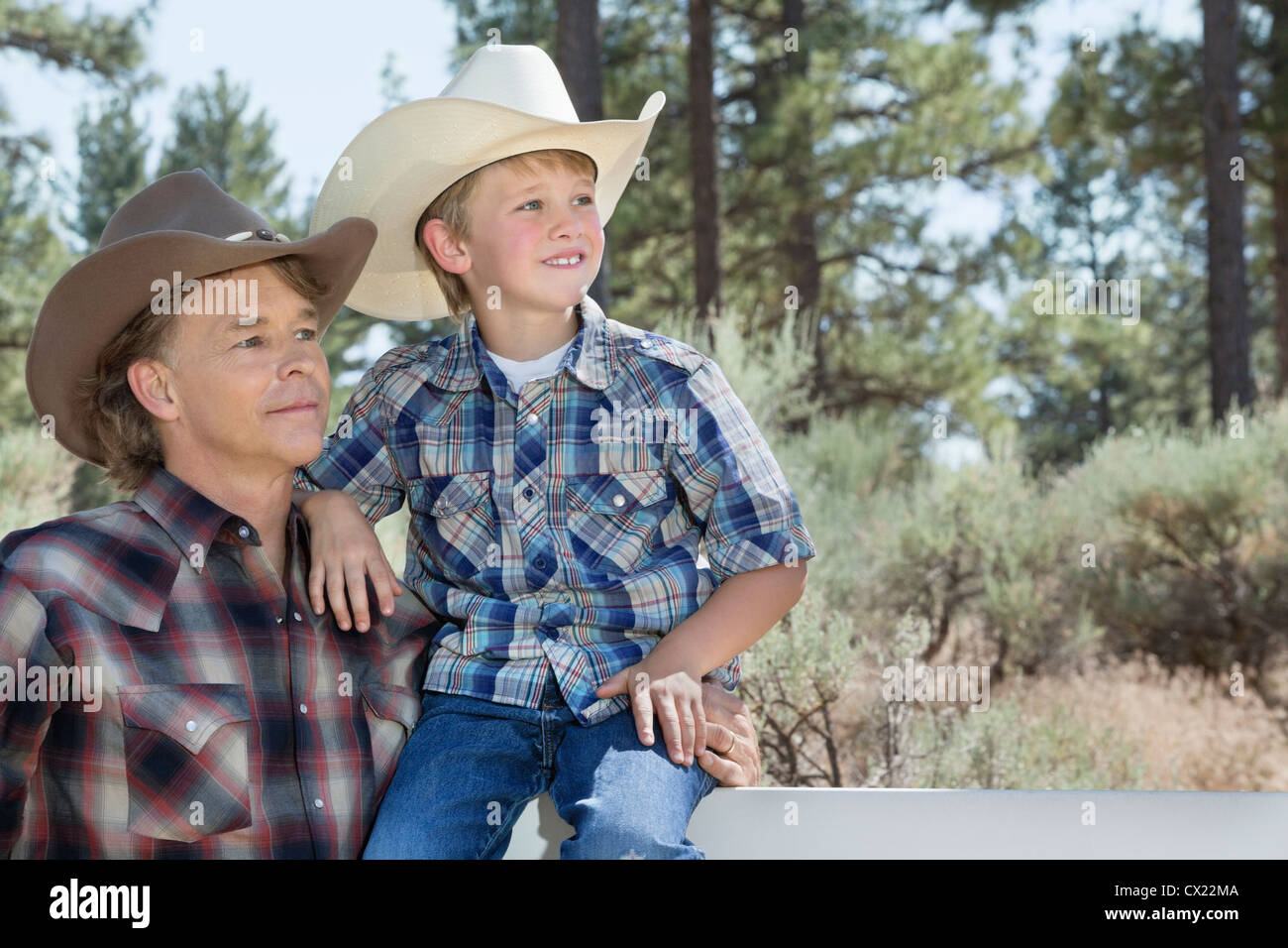 Mature father and son wearing cowboy hats looking away in park Stock Photo