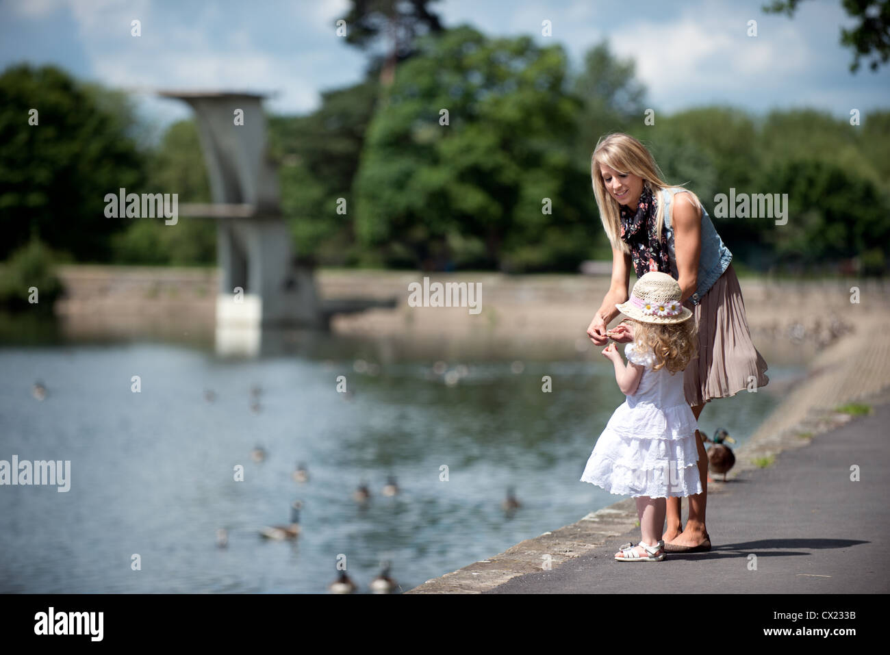A pretty young affluent mother enjoying feeding the ducks with her daughter at Coate Water country park, Swindon Wiltshire, UK Stock Photo