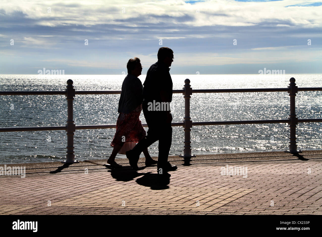 Couple walking on sea front in silhouette Stock Photo - Alamy