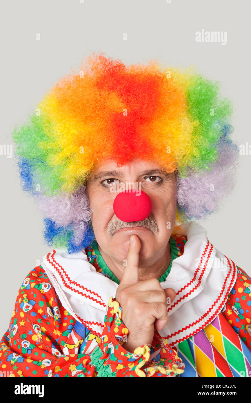 Portrait of angry senior male clown with finger on chin over light gray background Stock Photo