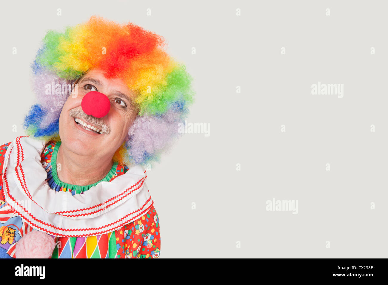 Happy senior clown looking up against gray background Stock Photo