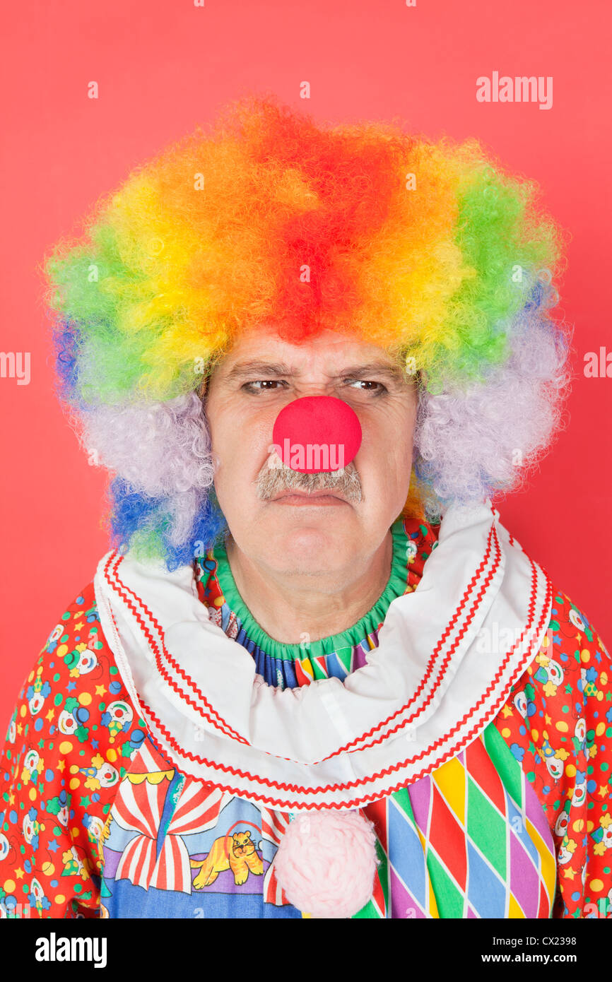 Senior male clown frowning over red background Stock Photo