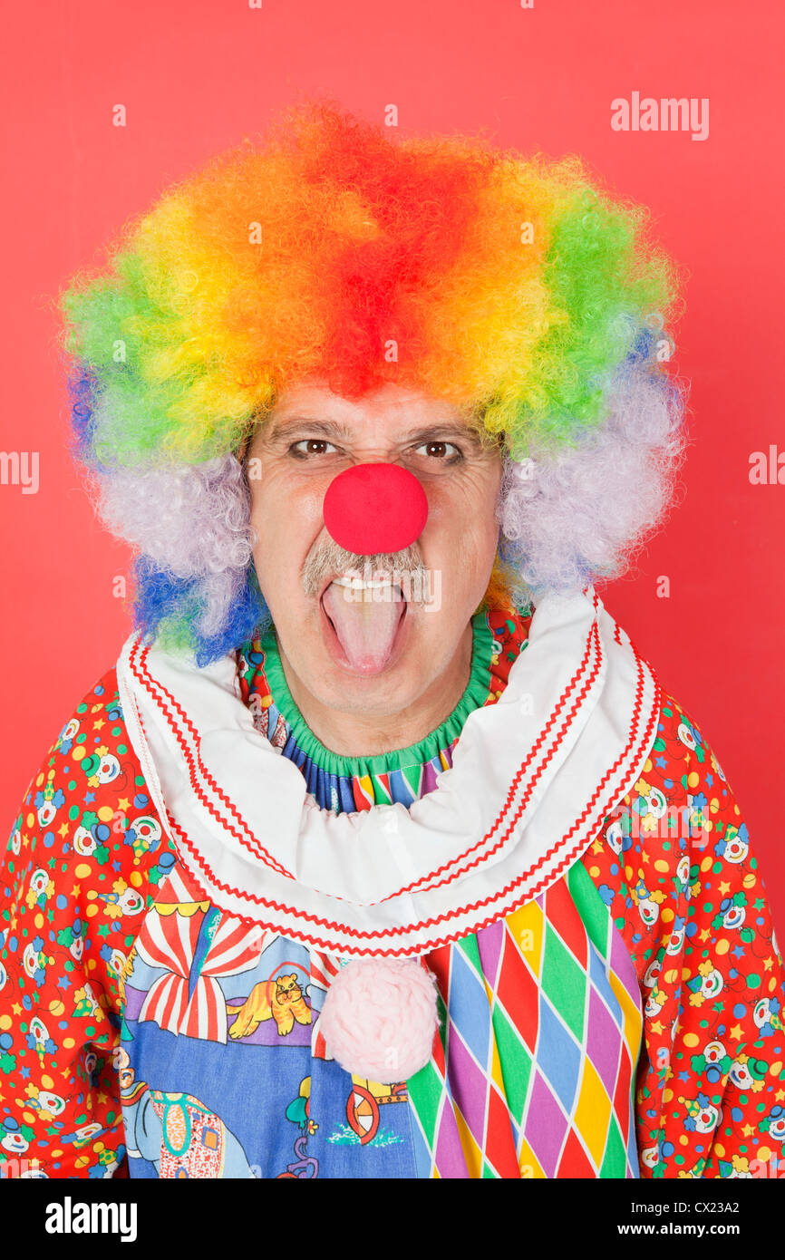 Portrait of senior male clown sticking out tongue over red background Stock Photo