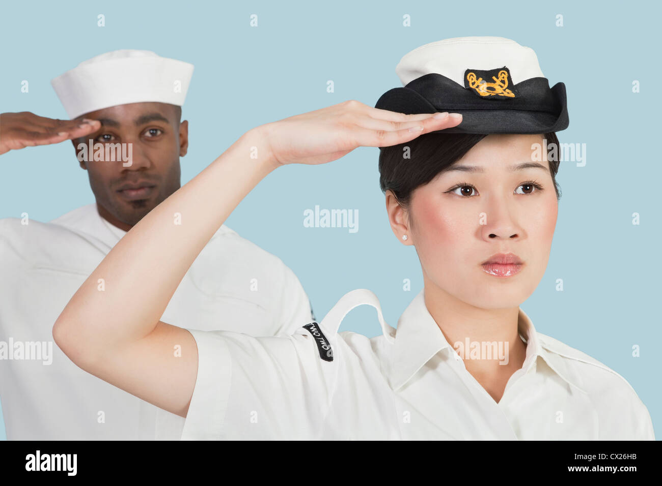 Portrait of serious female US Navy officer and male sailor saluting over light blue background Stock Photo