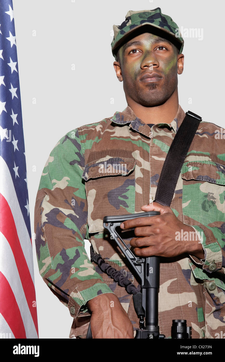 US Marine Corps soldier with M4 assault rifle standing by American flag over gray background Stock Photo